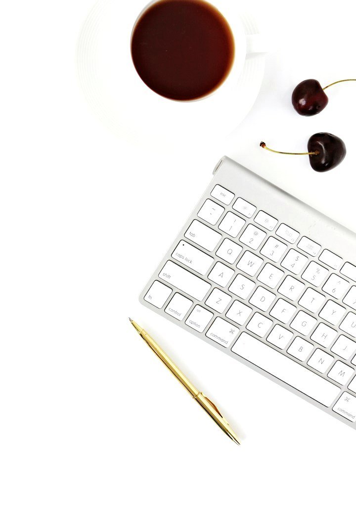 Vue du dessus : un clavier blanc, un stylo doré et une tasse de café sur un bureau blanc.